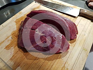 Big wild game meat cut in half on a wooden cuttingboard with big sharp kitchen knife