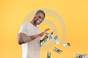 Big win, cashback, wealth concept. Young african american guy throwing out money bills, yellow background