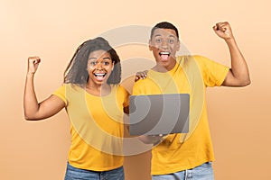 Big win concept. Overjoyed black couple holding laptop, cheering, celebrating victory and shaking clenched fists