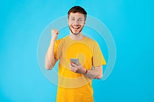 Excited man using smartphone at studio, celebrating online win