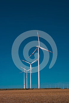 Big wind turbines to generate electrical power, green ecofriendly energy at blue sky standing in arid lifeless soil during sunset