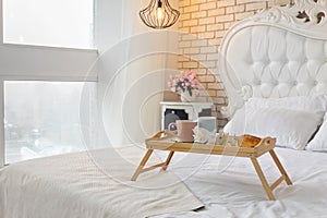 Big windows and white interior with two mugs on a tray with croissant and orchid flower on white luxury bed.Breakfast concept