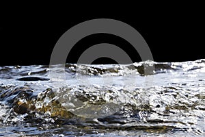 Big windy waves splashing over rocks. Wave splash in the lake on black background. Waves breaking on a stony beach, forming a spra