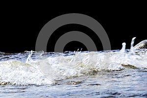 Big windy waves splashing over rocks. Wave splash in the lake isolated on black background. Waves breaking on a stony beach, formi