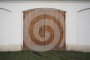 Big wooden barn gate. Monumental farm door, two timber leaf, closed brown gateway with planks and nails