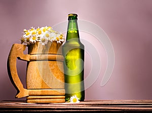 wooden beer mug with fine daisies similar to foam and a green full bottle with a metal lid