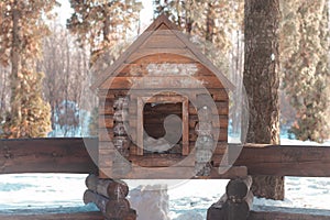 A big wooden birdhouse reminding a wooden rural house made with timber. During a snowy winter or spring in the woods of an urban
