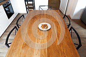 Big wooden table with chairs and cookies in the kitchen. Lonely white plate with cookies on an empty dinner table. Solid wooden
