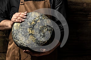 Big yellow cheese wheel in seller hands. cheese in man's cheesemaker hands. marble cheese