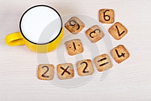 Big yellow cup of milk and funny cookies with numbers on light wooden background. Healthy breakfast for a child.