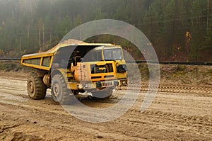 Big yellow diesel quarry dumper at work. Heavy mining truck transporting sand and clay