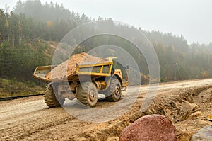 Big yellow diesel quarry dumper at work. Heavy mining truck transporting sand and clay.