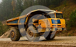 Big yellow diesel quarry dumper at work. Heavy mining truck transporting sand and clay.
