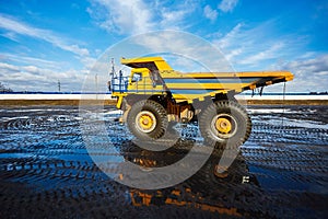 A big yellow dump truck is standing in the mud against the blue sky