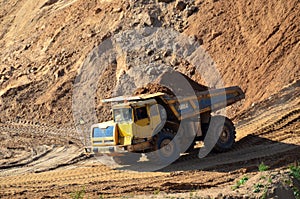 Big yellow dump truck transporting sand in an open-pit mining quarry.