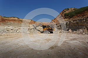 A big yellow excavator on a new construction site on the blue sky and sandy quarry background. Copy space. Copy space.