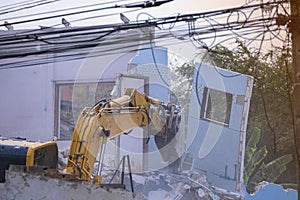 Big yellow excavator removal home building by destroy blue concrete wall. uproot old construction house for development new photo