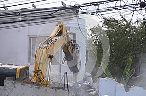 Big yellow excavator removal home building by destroy concrete wall. uproot old construction house for development new project photo