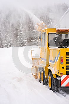 Big yellow snowplough with and helix is cleaning the road while a powerful stream of white snow go out