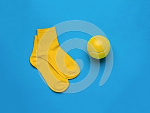 A big yellow tennis ball and yellow socks on a blue background. Flat lay