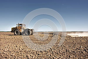 Big yellow tractor equipped with harrow working on the field