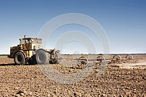 Big yellow tractor equipped with harrow working on the field