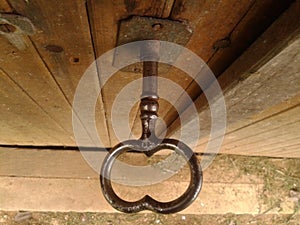 Bigger old worn black shiny key in oak wooden dusty cellar door, close-up from above, in daylight