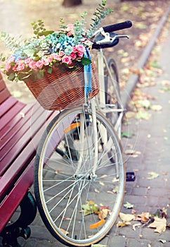 Bike with flowers basket in park near bench. Tone image .