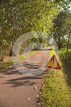 Bike lane in the countryside with trees and street lights and a danger sign on the ground on a clear day in summer