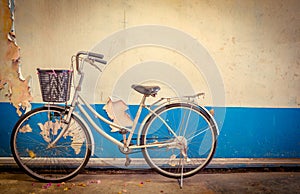 The bike parked next to the old white and blue peeling paint concrete wall