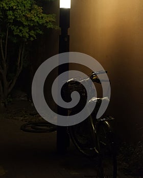 Bike parked on the side of a dimly lit street, resting against a wall.