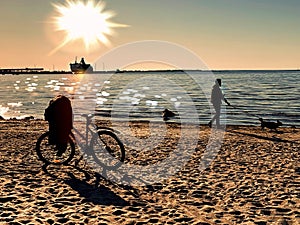 Bike  and people  silhouettes  walking  on the beach sand at  summer sunset on sea on skyline ,reflection of sunlight on wa of sun