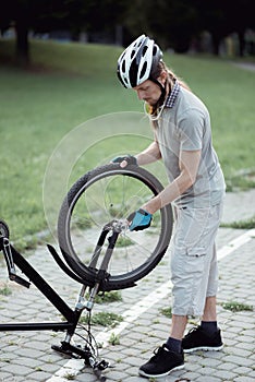 Bike repair. Young man repairing mountain bike in the park