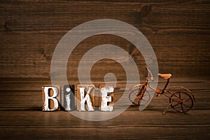 BIKE. Text from alphabet blocks and rusty miniature bicycle on wood texture background