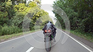 Biker is accelerating at motorcycle on empty country road. Man riding fast on modern sport motorbike at forest route