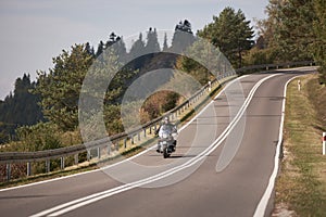 Biker in black leather outfit driving modern powerful motorcycle along sunny road on summer day.