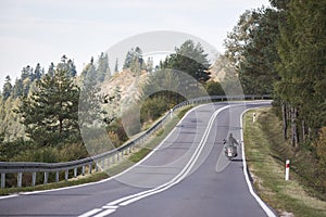 Biker in black leather outfit driving modern powerful motorcycle along sunny road on summer day.