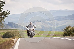 Biker in black leather outfit driving modern powerful motorcycle along sunny road on summer day.