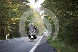 Biker in black leather outfit driving modern powerful motorcycle along sunny road on summer day.