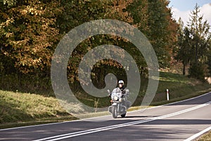 Biker in black leather outfit driving modern powerful motorcycle along sunny road on summer day.