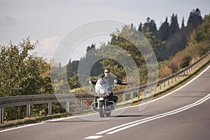 Biker in black leather outfit driving modern powerful motorcycle along sunny road on summer day.