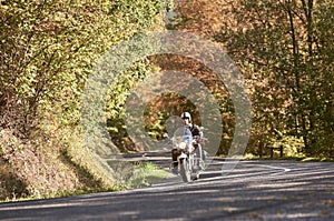 Biker in black leather outfit driving modern powerful motorcycle along sunny road on summer day.