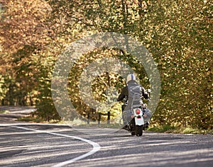 Biker in black leather outfit driving modern powerful motorcycle along sunny road on summer day.