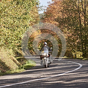 Biker in black leather outfit driving modern powerful motorcycle along sunny road on summer day.