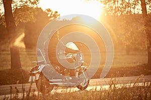 Biker in black leather outfit driving modern powerful motorcycle along sunny road on summer day.