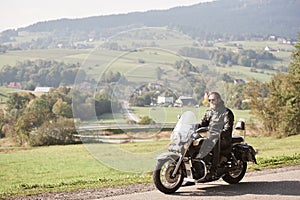 Biker in black leather outfit driving modern powerful motorcycle along sunny road on summer day.