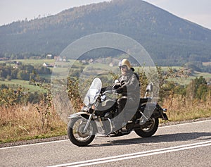 Biker in black leather outfit driving modern powerful motorcycle along sunny road on summer day.