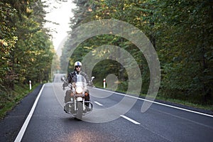 Biker in black leather outfit driving modern powerful motorcycle along sunny road on summer day.