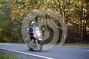 Biker in black leather outfit driving modern powerful motorcycle along sunny road on summer day.