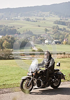 Biker in black leather outfit driving modern powerful motorcycle along sunny road on summer day.